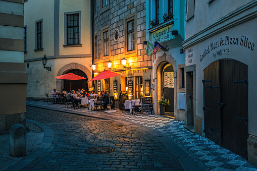 Prague, Czech Republic - June 28, 2023: Small outdoor restaurant on the narrow cobblestone street illuminated by lights in old town of Prague - capital of Czechia, famous and popular travel destination.