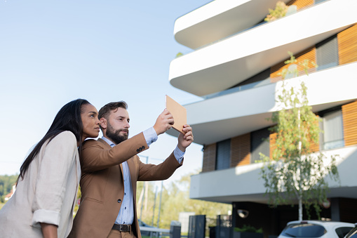 Real estate agent and client taking photos of apartments with a tablet at commercial or residential property, they looking at blueprints and  discussing about prises, apartments, properties of apartments, quality of construction, arrangement of new apartments. A real estate agent takes photos of a property.