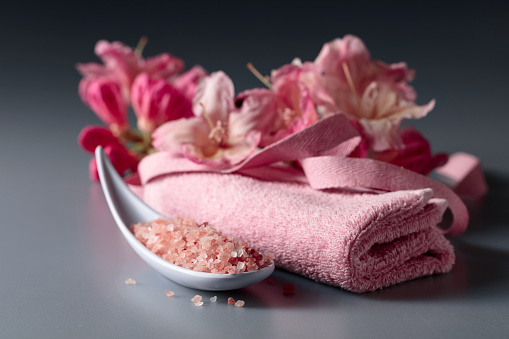 Spa composition with pink Himalayan salt, flowers, and towel.