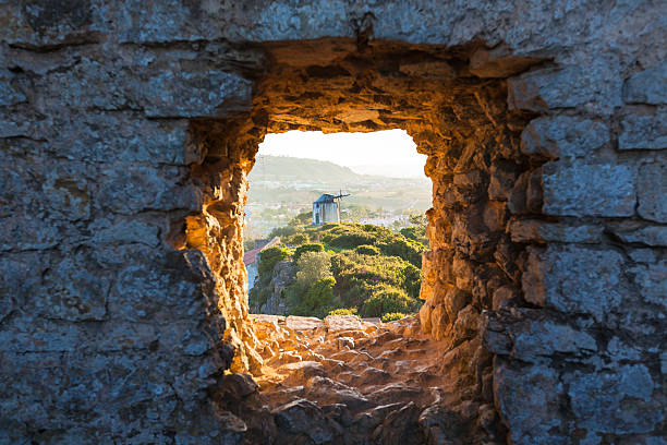 Old Windmill through Window in Fortress Wall Old Windmill through Small Window in Obidos Fortress Wall, Portugal. Evening Sunlight obidos photos stock pictures, royalty-free photos & images