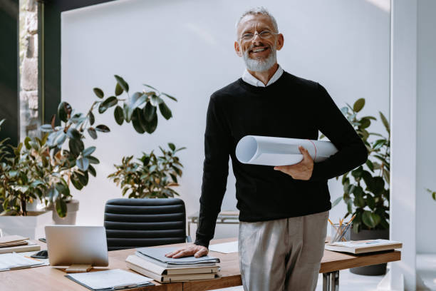 istock Happy mature architect carrying blueprint and looking at camera while standing in the creative office 1671295521