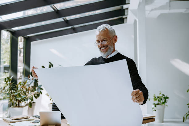 istock Confident mature engineer examining blueprint and smiling while standing in the creative office 1671297110