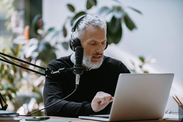 istock Confident mature presenter recording podcast while looking at computer monitor in studio 1671297623