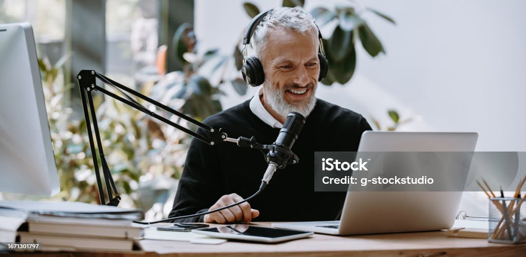 Podcaster Using A Microphone Cheerful Mature Podcaster In Headphones Using Microphone While ...