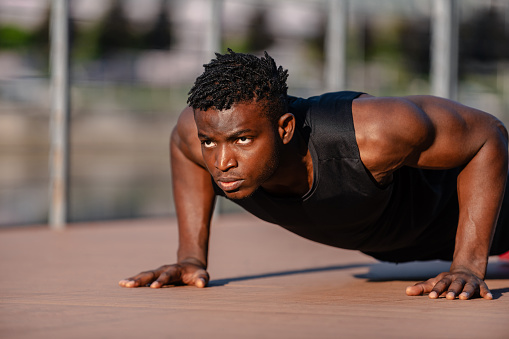 Confident young African athlete in sportswear doing push-ups while exercising outdoors