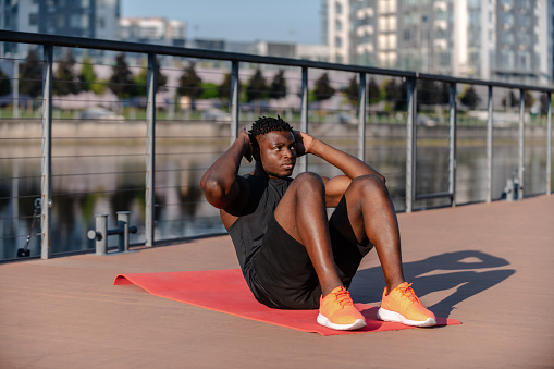 Confident young African man in sportswear doing sit-ups while exercising on mat outdoors