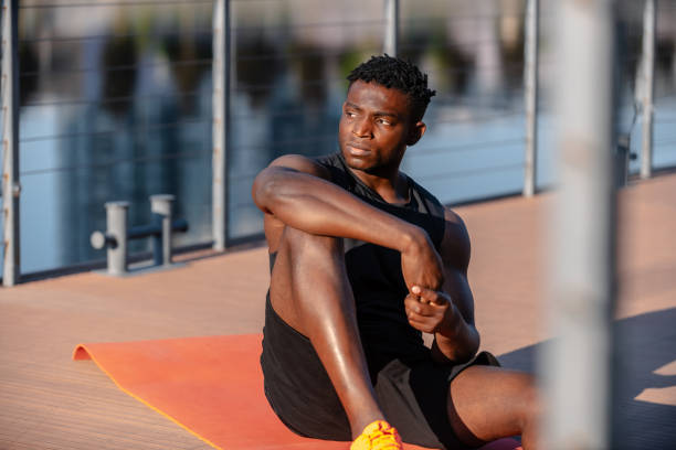 istock Handsome young African man in sportswear resting after training while sitting on exercise mat outdoors 1671321047