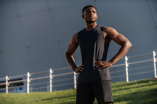 Confident African man in sportswear holding hands on hip while training outdoors