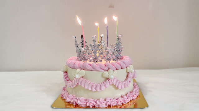 A birthday cake with candles with lights and a beautiful silver crown.