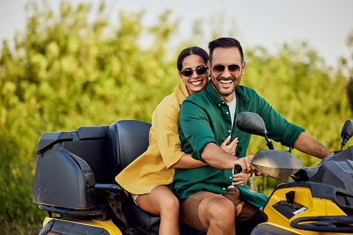 A happy love couple sitting on a rental quad bike and having an adventure through beautiful nature, smiling for the camera.