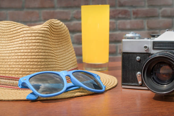 Camera with blue sunglasses and hat on wooden table