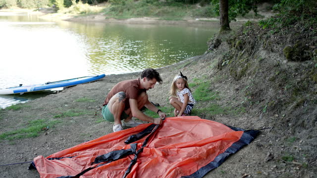 Father and daughter are setting up a tent