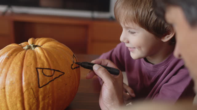 Father and his little boy painting and carving Jack O' Lantern pumpkins for Halloween