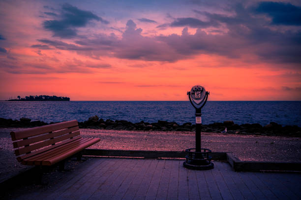 Milford Connecticut Sunset Seascape with an empty bench and a viewing scope at Silver Sands State Park, Charles Island view on Long Island Sound Beach