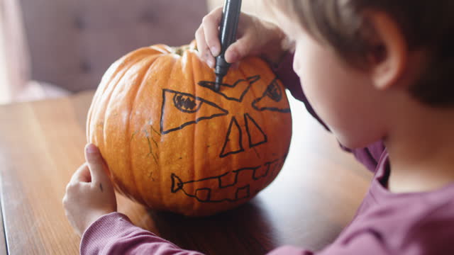 Cute little boy preparing Jack O' Lantern pumpkin for Halloween at home