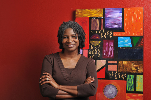 Portrait of middle-aged lovely black womanin front of one of her paintings