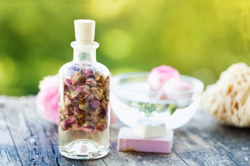 glass  bottlel with massage oil with dried rose buds, soap bar  and a pink rose on rustic weathered wood