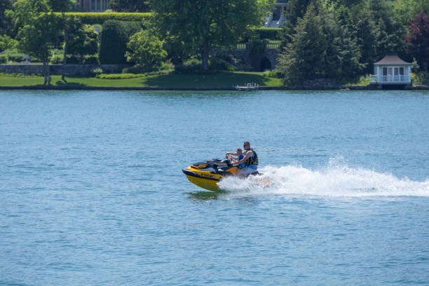 Father and son on a jet ski on Skaneateles Lake in New York State.  Sunny summer day with shoreline in view.