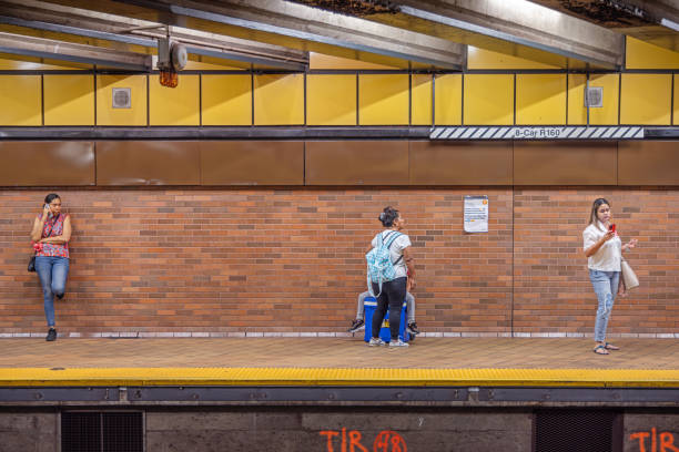 21th Street Queensbridge Subway Station, Long Island City, Queens, New York, USA - August 21th 2023:  People with mobile phones waiting for the subway train standing on the platform at the underground station