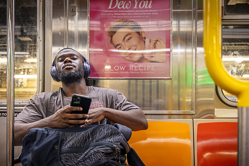 New York Subway, New York, USA - August 15th 2023:  Man sitting in a subway car listening to music from his mobile phone