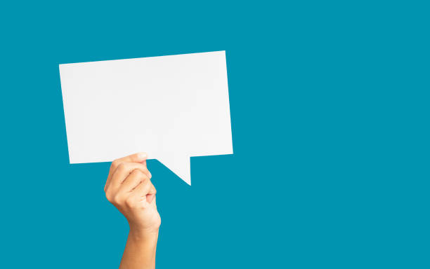 istock Close-up of hand holding a white speech bubble against a blue background 1671582669