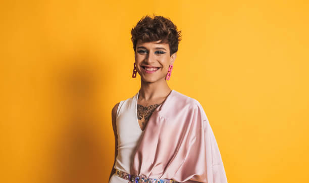 non binary person with pink clothes and make up smiling at the camera on yellow stock photo