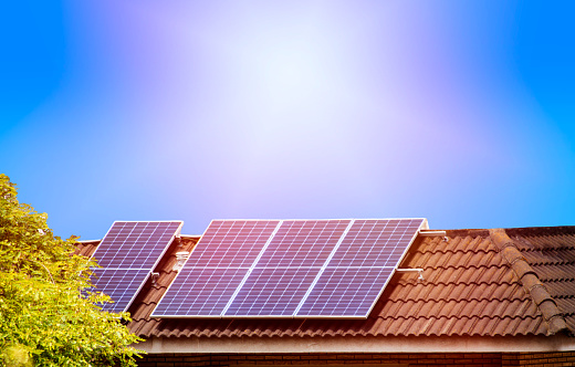 Solar panels on the tiled roof of the house in the sun. Electricity production for own needs and for sale with copy space.