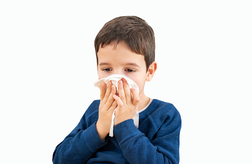 Child blowing in a wipe suffering flu symptoms with white background.