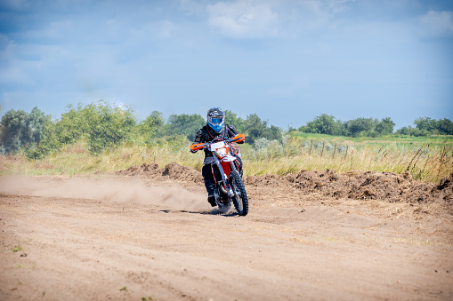Motorsport photograph of a motocross rider in red sportswear riding his motorcycle on a dirt track in forest
