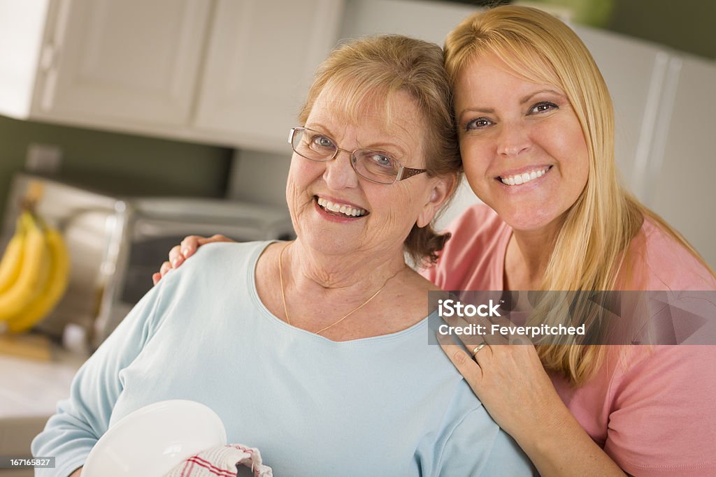 Senior Adult Woman and Young Daughter Portrait in Kitchen Smiling Senior Adult Woman and Young Daughter At Sink in Kitchen. 40-49 Years Stock Photo