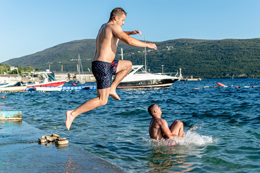 This image signifies waves of happiness as two friends jump into the water, embracing the joyful experience