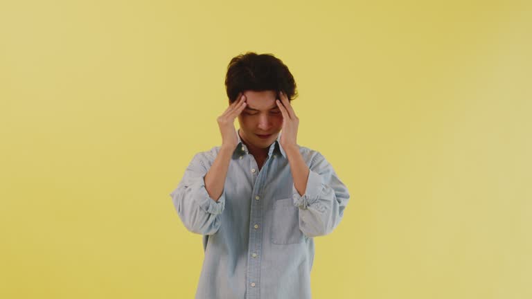 A man with stress and depression with his hand on his head isolated on a yellow background.