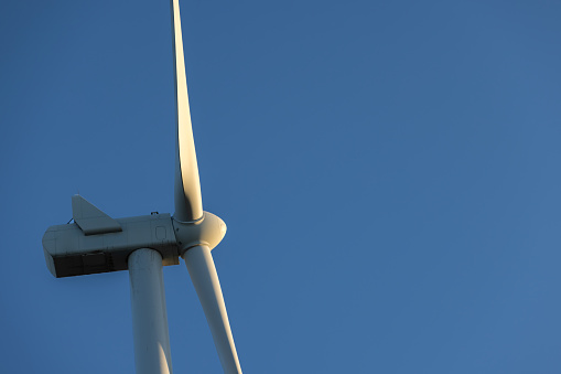 Close-up in aerial view at large propeller of windmill, wind generator, turbine, in background is field for producing renewable clean energy by converting kinetic energy on agricultural ground.
