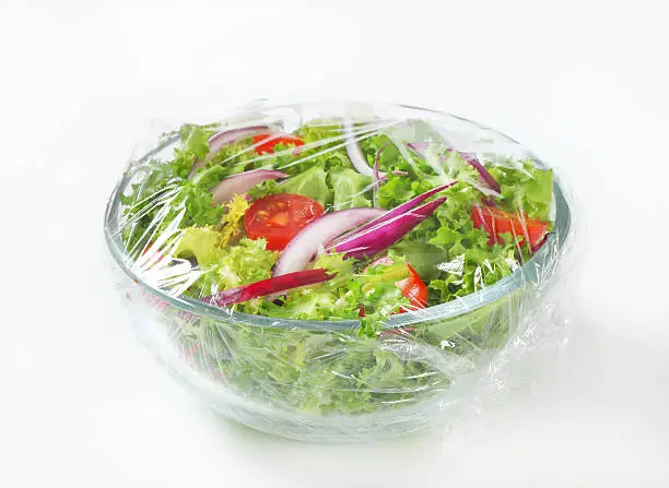 fresh vegetable salad in a glass bowl covered with plastic wrapping film