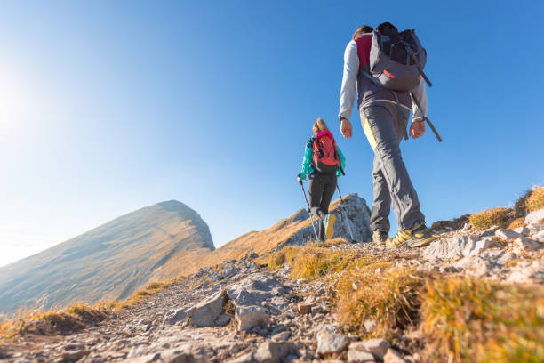 istock Two hikers walking along a mountain ridge route, the sun on the blue sky 1671726666