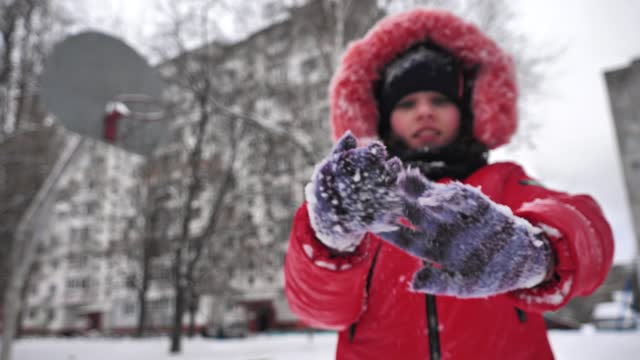 Slow motion video of a teenage girl cleans her gloves from snow.