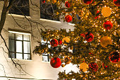 A Christmas tree decorated with New Year's toys against the background of a house wall with windows.