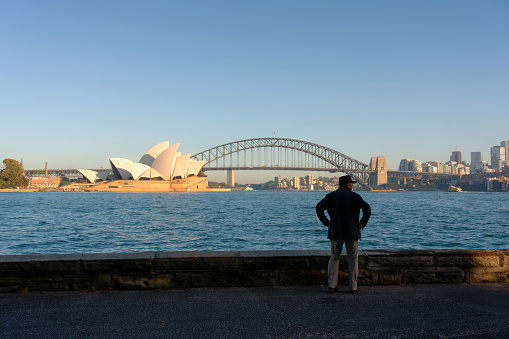 Sydney Australia - August 29, 2023: Sporting an Indiana Jones-style hat, a man in his fifties takes in the wonders of Sydney Harbour including the iconic Opera House and Harbour Bridge.