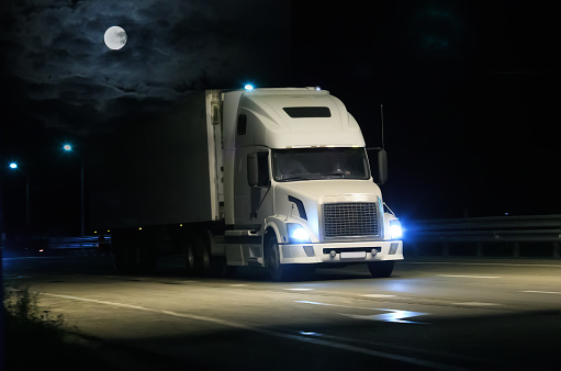 Large Truck drives along a suburban highway on a moonlit night.