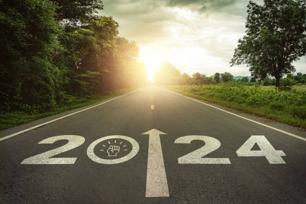 istock 2024 New Year, team motivation, encourage, collaboration concept. Teamwork, empowerment for achieving success. 2024 written and teamwork icons on the road in the middle of asphalt road with at sunset. 1671859741