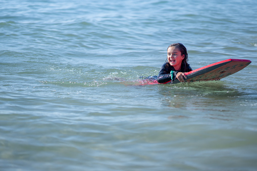 A little girl floats on her board as she waits for the next big wave to come in.  She is wearing a swimsuit and smiling as she enjoys the fresh summer air.