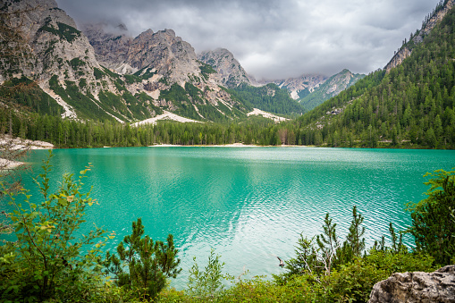 Braies lake surrounded by pine forests and the rocky ranges of the Dolomites in cloudy day, Italy. High quality photo