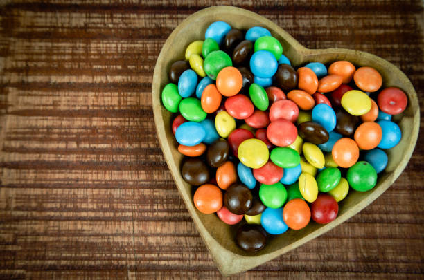 pila de coloridos dulces de chocolate en cuenco de madera en forma de corazón aislado sobre fondo blanco, vista superior - chestnut sweet food yellow group of objects fotografías e imágenes de stock