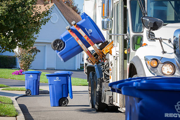 Recycling Truck Lifting Up Container Along Neighborhood Curb A recycling truck in a residential neighborhood is shown using it's mechanical arm to lift up a blue container containing recyclable materials. Other containers can be seen along the curbside. Canon 5D MarkII.  curb photos stock pictures, royalty-free photos & images