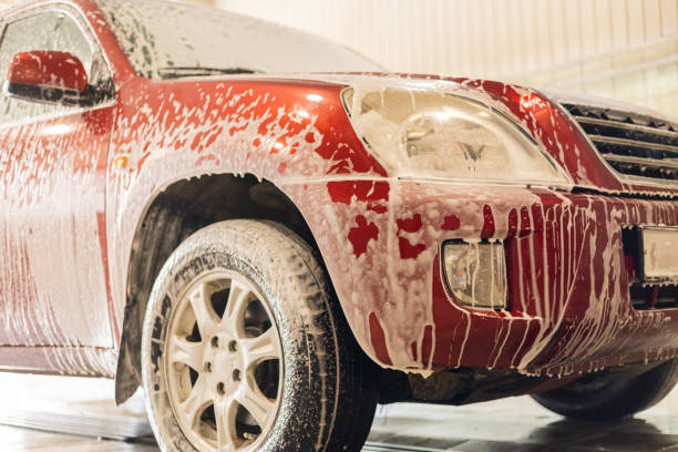 al lavandino, la schiuma scorre verso il basso e gocciola dall'auto sul pavimento della scatola. l'auto è stata portata al lavandino per pulire lo sporco e la polvere dopo la strada. il concetto di autolavaggio senza contatto. - fountain water physical pressure splashing foto e immagini stock