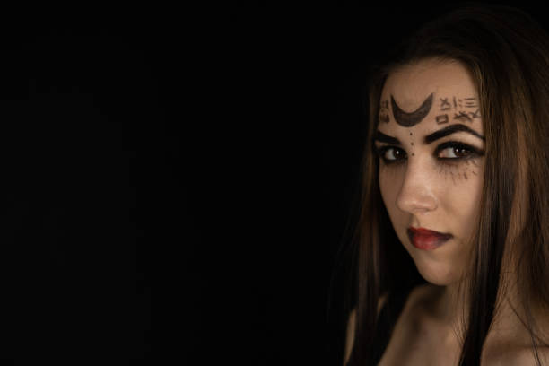 istock Copy space. On a black background, a beautiful witch looks at the camera and smirks. Halloween. Portrait. At night, in the dim light, a woman in the form of a witch laughs. 1671946210