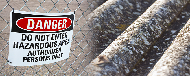 Dangerous presence of asbestos fibers in a construction site with metallic protection net against the intrusion of unauthorized persons and warning signboard