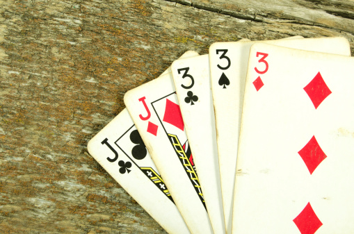 A poker  hand of old used  cards showing a full house. On a well worn barn board with lichen.
