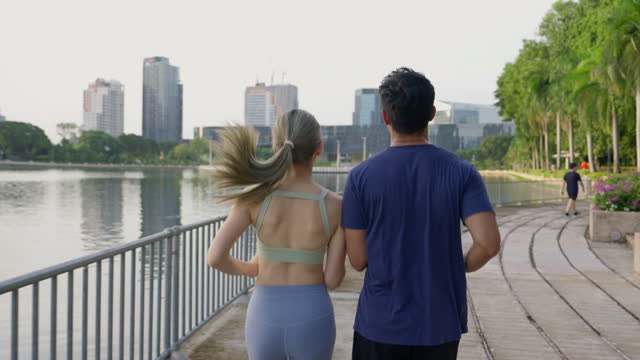 A couple is seen exercise and jogging together in a park with enjoying the city fresh air and scenic views and prioritizing exercise and good health during the holidays.