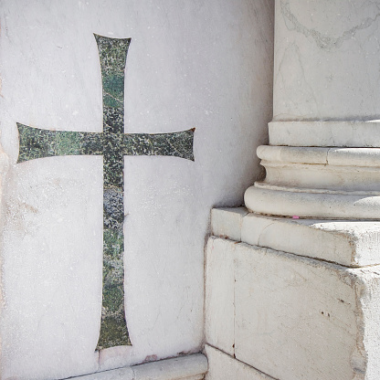 Old italian church with metal catholic Christian cross against a white stone wall